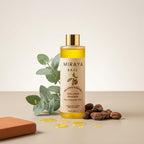 Bottle of Miraya Golden Jojoba oil with jojoba beans and eucalyptus leaves on a beige background