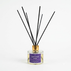 Lavender Dusk reed diffuser with a clear glass bottle, purple label, and black reeds with a gold cap, on a white background.